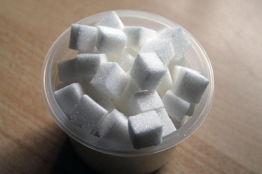 Ein Becher gefüllt mit weißen Zuckerwürfeln – symbolisch für übermäßigen Zuckerkonsum und die Motivation, Zucker im Alltag zu reduzieren für eine bessere Gesundheit.
